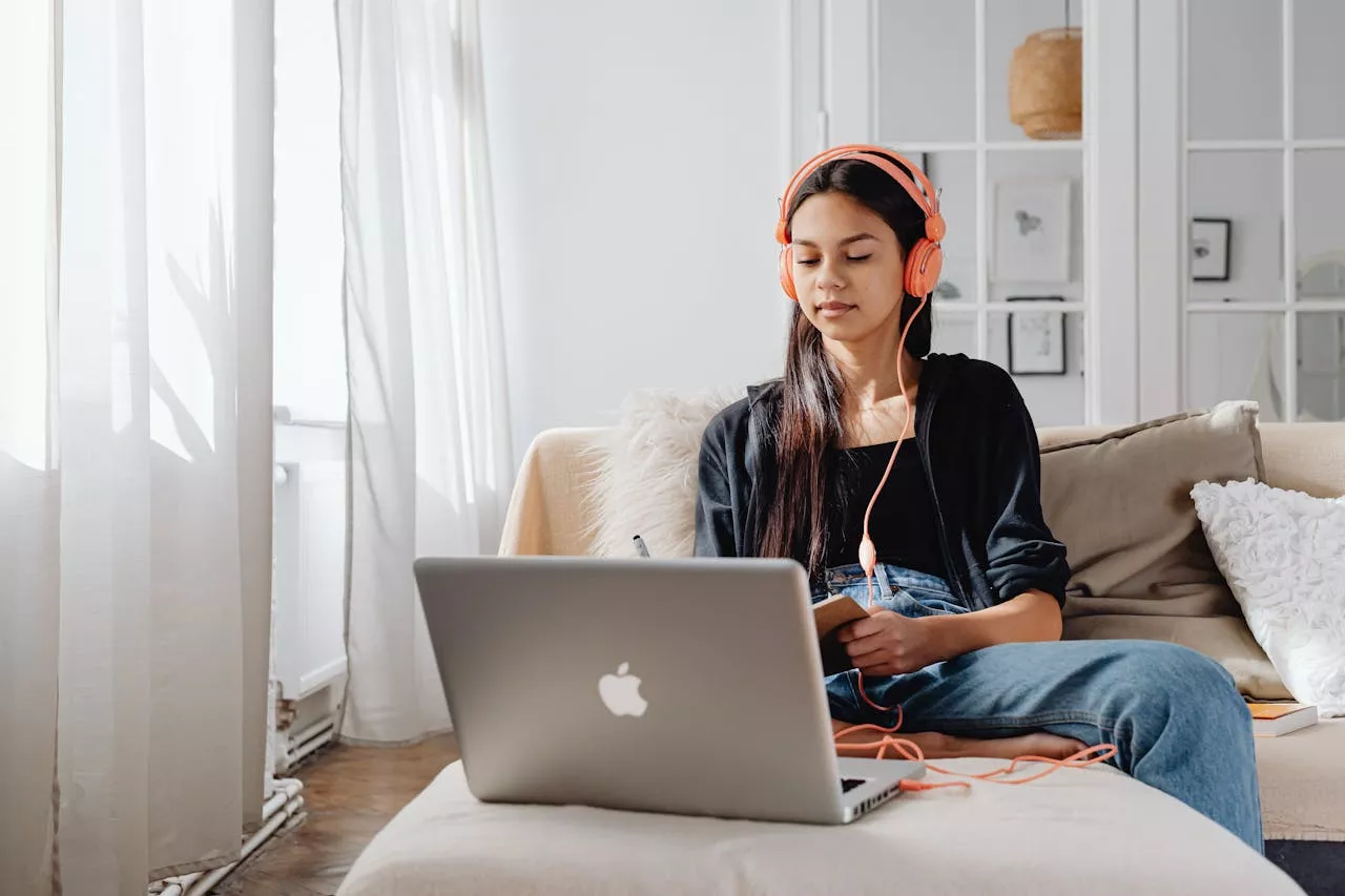vision Teenage girl wearing headphones using a laptop for online learning at home in a cozy setting.