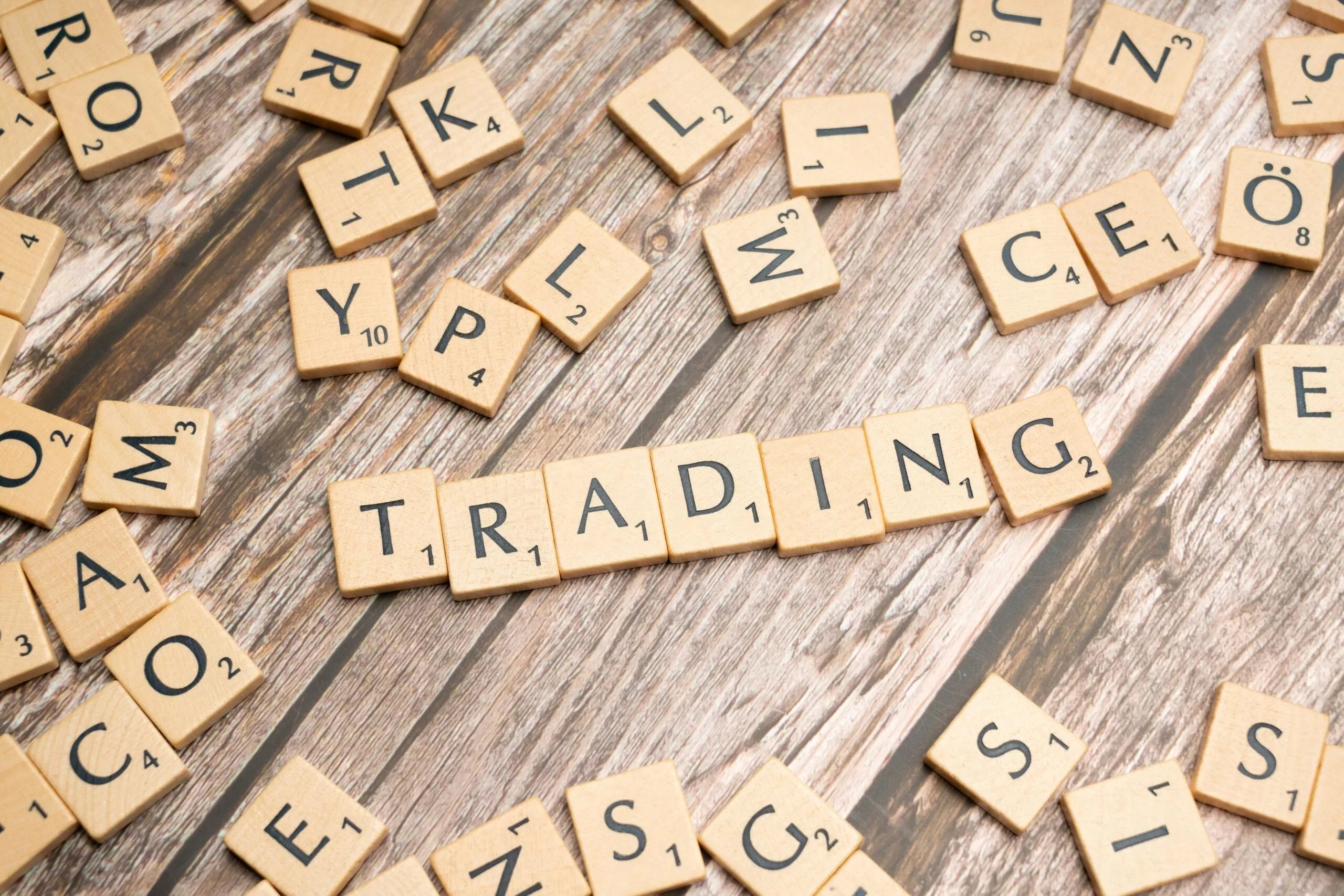 Wooden Scrabble tiles spelling 'TRADING' against a rustic wood background.